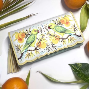 May include: A white clutch bag with a scalloped edge, featuring a colourful illustration of two green parrots on a branch with oranges. The bag has a yellow tassel and a light green interior.