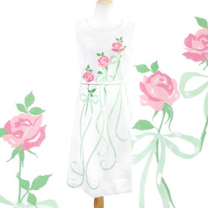 May include: A white sleeveless dress with a green and pink floral pattern. The dress has a fitted bodice and a full skirt. The floral pattern features pink roses and green leaves with green ribbons tied in bows.