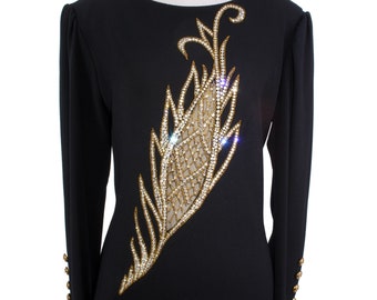 Könnte beinhalten: Ein schwarzes Kleid mit langen Ärmeln und einem großen goldenen und klaren Strass-Feder-Design auf der Vorderseite.