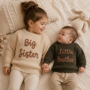 May include: A beige knit sweater with the text Big Sister in brown embroidery and a dark olive green knit sweater with the text little brother in brown embroidery, both featuring long sleeves and a crew neckline.