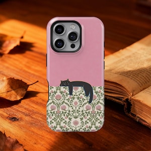 May include: A pink phone case featuring a black cat lounging on a floral pattern. The case has a two-tone design, with a solid pink top and a patterned bottom. The floral design includes pink flowers and green leaves.