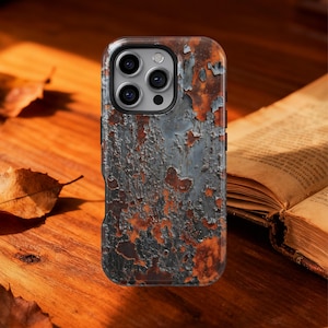 May include: A phone case with a distressed, weathered appearance. The case has a textured surface with peeling paint in grey, brown, and orange hues. It features a camera cutout and black side buttons. The case is set on a wooden surface.