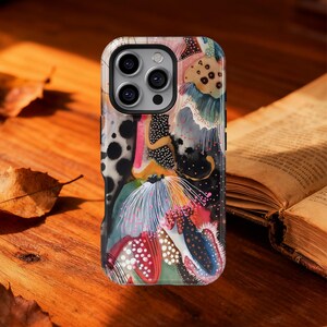 Puede incluir: Una funda para smartphone con un diseño abstracto multicolor que presenta formas orgánicas, puntos y patrones de líneas finas en negro, blanco, rosa y turquesa. La funda tiene un recorte para la cámara que muestra tres lentes circulares.