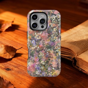 May include: A floral phone case featuring a colorful pattern of small flowers in shades of pink, purple, white, and yellow. The case has a black border and a camera cutout. The case is on a wooden surface.