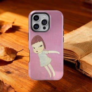 May include: A pink phone case featuring a cartoon illustration of a girl with a stern expression and outstretched arms. The artwork has a minimalist style with a light blue dress and brown hair. The case is shown on a wooden surface.
