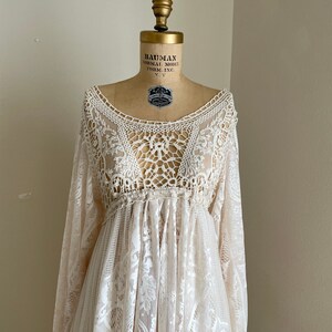 close-up of the intricate crochet bodies of A lace maxi wedding dress with long sleeves and a gathered waist. The dress has a delicate floral pattern and fringe bell sleeves
