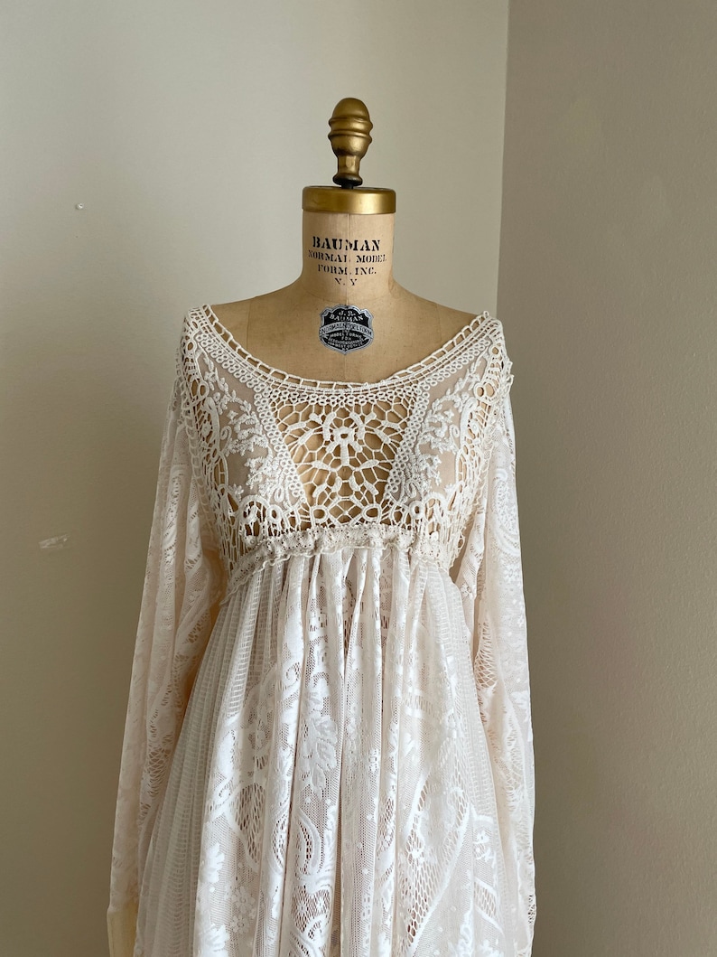 close-up of the intricate crochet bodies of A lace maxi wedding dress with long sleeves and a gathered waist. The dress has a delicate floral pattern and fringe bell sleeves