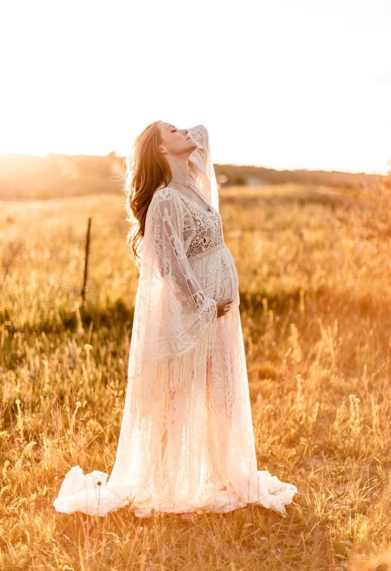 actual pregnant bride, wearing a long ivory lace, Bohemian wedding gown with long bell sleeves that have fringe and an extra long maxi skirt