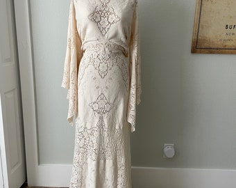 May include: A white lace maxi dress with long sleeves and a V-neckline. The dress has a fitted bodice and a flowing skirt.