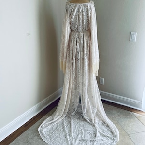 Full back view of long ivory lace, BoHo wedding dress that has Bell sleeves with fringe