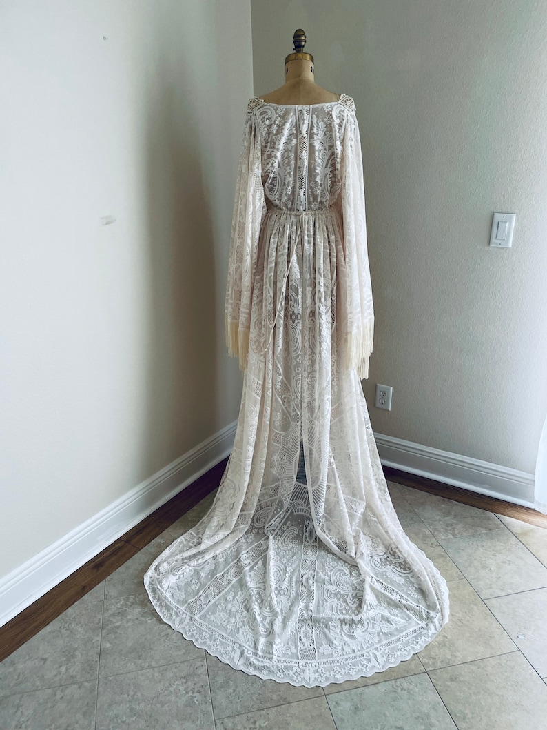Full back view of long ivory lace, BoHo wedding dress that has Bell sleeves with fringe