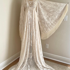 An ivory lace bohemian wedding dress with long bell sleeves that have long fringe. This scone has a crocheted bodice and long draped maxi skirt.