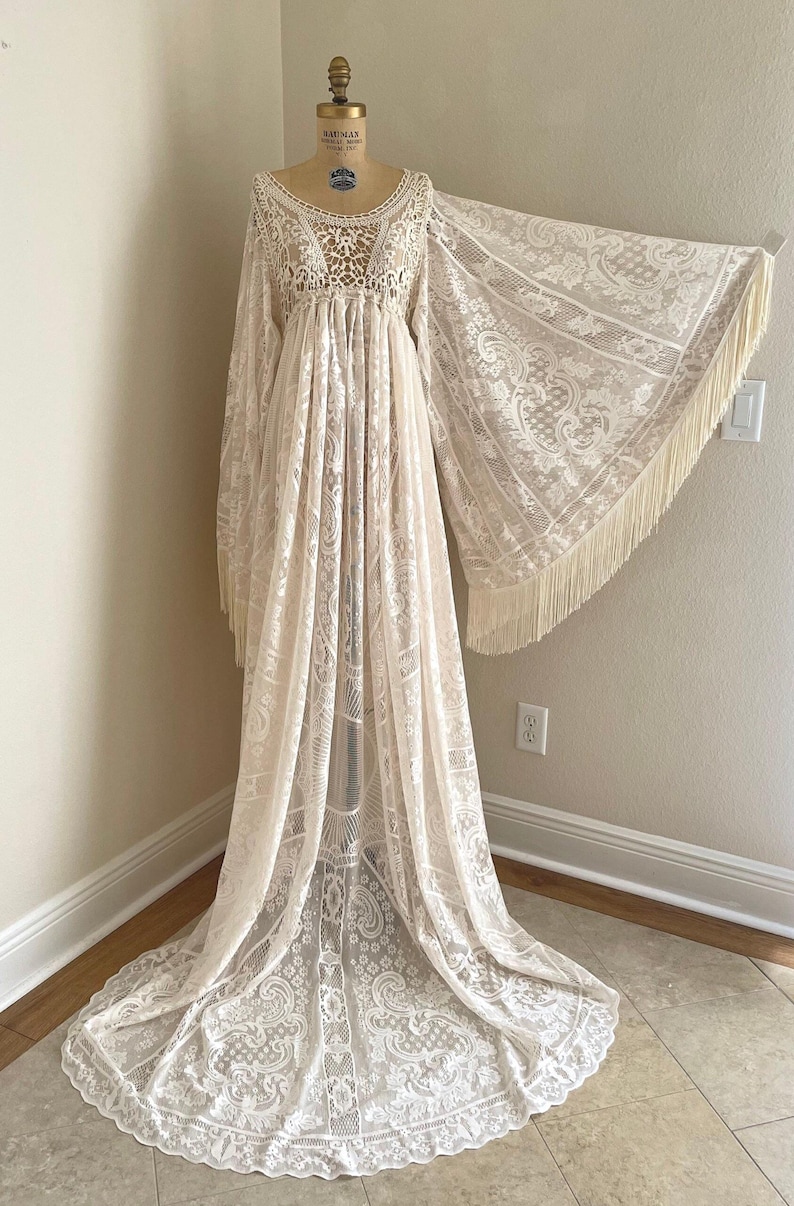 An ivory lace bohemian wedding dress with long bell sleeves that have long fringe. This scone has a crocheted bodice and long draped maxi skirt.