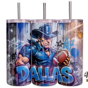 May include: Three stainless steel tumblers with a vibrant graphic. The design shows a strong cowboy with a football, and the word "DALLAS" in blue graffiti. The background has a graffiti art style, with blue and grey tones.