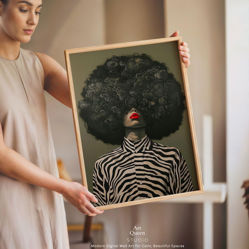 May include: A framed art print featuring a stylized portrait of a person with a large, dark, curly afro and red lipstick. The person is wearing a black and white zebra-striped shirt. The artwork is labeled "Art Queen Studio."