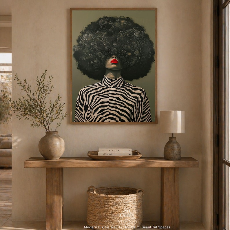 May include: A framed art print featuring a stylized portrait of a person with a large, curly afro. The person wears a black and white zebra-striped shirt and has bright red lipstick. The artwork is displayed above a wooden console table.