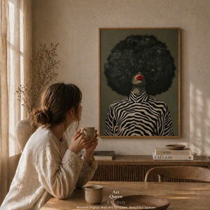 May include: A framed art print featuring a woman with a large afro and red lipstick, wearing a black and white zebra-striped shirt. The artwork is displayed in a room with a woman holding a mug. The text "Art Queen Studio" is visible.