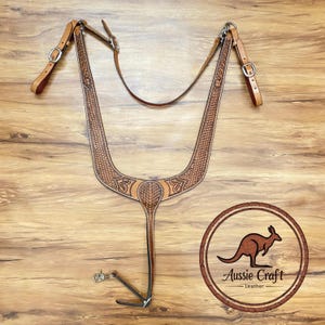 Puede incluir: Un petral de cuero marrón claro para caballos con repujado decorativo. El petral tiene correas ajustables y herrajes metálicos. La imagen también incluye un logotipo con un canguro y el texto "Aussie Craft Leather".