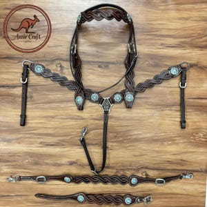 Könnte beinhalten: Aussie Craft Leder-Pferdegeschirr-Set. Das Set beinhaltet einen geflochtenen Lederzaum, einen Brustgurt und weiteres Zubehör. Das braune Leder ist mit türkisfarbenen Verzierungen und silberfarbener Hardware versehen. Das Logo zeigt ein Känguru.