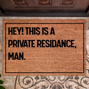 May include: A rectangular doormat with a brown, textured surface and a black border. The mat features the phrase "HEY! THIS IS A PRIVATE RESIDANCE, MAN." in bold, black letters. The mat is placed in front of a door.