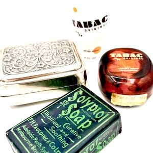 May include: A collection of vintage grooming products, including a silver box with decorative patterns, a bottle of Tabac aftershave, a jar of Tabac luxury soap, and a bar of Solyptol soap. The Solyptol soap is in a green and black wrapper.