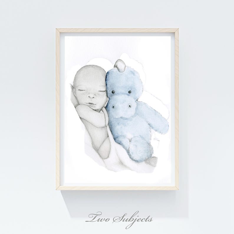 May include: Watercolor print of a sleeping baby and a blue stuffed hippo. The baby is in grayscale, and the hippo is light blue. The print is framed in a light wood frame. The text "Two Subjects" is at the bottom.