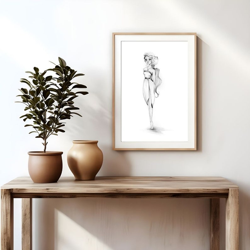 Op de afbeelding: Een zwart-witte potloodtekening van een vrouw in een vloeiende jurk, ingelijst in een licht houten lijst en hangend aan een witte muur.