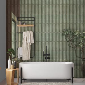 May include: A modern bathroom with a white bathtub, black fixtures, and a green tiled wall. A wooden side table holds toiletries and a plant. A black towel rack holds a robe and towels. A large plant is in a red pot.