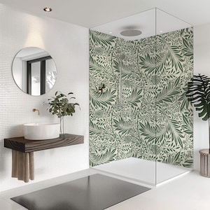 May include: A modern bathroom with a glass-enclosed shower featuring a green and cream floral pattern. The room includes a white sink on a wooden shelf, a round mirror, and a black floor mat. A potted plant adds a natural touch.