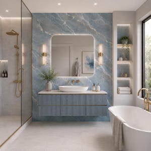 Pode incluir: Uma casa de banho moderna com uma parede com efeito mármore azul e um espelho grande e iluminado. Apresenta uma bancada azul com detalhes dourados, uma pia oval branca, uma banheira independente e um box de duche de vidro com acessórios dourados.