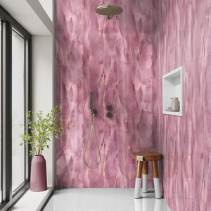 May include: A modern bathroom with a pink, textured wall design featuring gold accents. The shower area includes a showerhead, handheld shower, and a small wooden stool with white-tipped legs. A vase with greenery sits by a large window.
