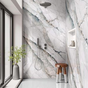 May include: A modern bathroom with a marble-patterned shower wall. The shower features a rain shower head and a handheld shower. A wooden stool with white-tipped legs sits on the tiled floor. A tall gray vase with greenery sits near a large window.