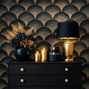 May include: A black dresser with gold knobs holds a navy blue vase with gold fern and blue flowers, gold candles, and navy blue boxes. A gold lamp with a black shade sits next to the boxes. The background is a black and gold fan pattern.
