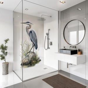 May include: A modern bathroom with a glass shower enclosure featuring a large blue heron illustration. The shower has a rain shower head and handheld shower. A black sink and round mirror are also visible.
