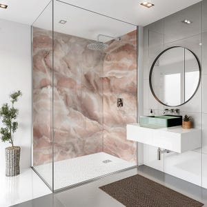 Może przedstawiać: Nowoczesna łazienka z szklaną kabiną prysznicową z różowo-białą ścianą imitującą marmur. Prysznic ma srebrną głowicę. Widoczna jest również biała toaletka z zieloną szklaną umywalką i okrągłym lustrem.