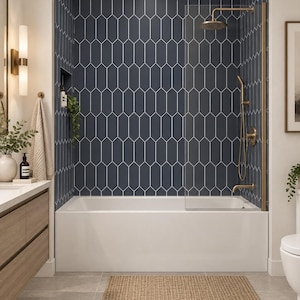 Op de afbeelding: Een badkamer met een wit bad, een glazen douchescherm en een messing douchearmatuur. De muur achter het bad is betegeld met donkerblauwe, langwerpige zeshoekige tegels. Een geweven rechthoekige mat ligt op de lichtgrijze tegelvloer.