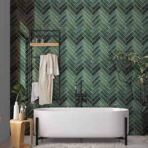 May include: A modern bathroom featuring a white oval bathtub with black legs. The wall is covered in green herringbone tiles. A black towel rack holds a robe and towels. A small wooden side table holds toiletries.