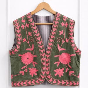 Può includere: Gilet verde oliva con ricami floreali rosa. Il gilet senza maniche presenta uno scollo a V ed è foderato con tessuto a righe bianche e nere. Il ricamo comprende fiori e motivi a foglie.
