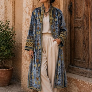 May include: A long, blue velvet duster coat featuring intricate gold floral embroidery and geometric patterns along the collar and cuffs. The coat is worn over a light beige, sleeveless top and matching wide-leg trousers, paired with brown sandals.