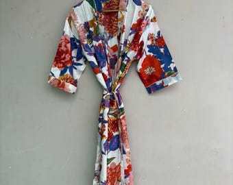 May include: A white floral print robe with a tie closure. The robe features a vibrant pattern of red, blue, purple, and yellow flowers. The robe is hanging on a wooden hanger against a neutral background.