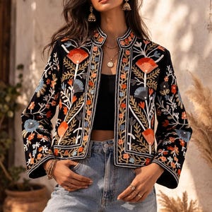 Peut inclure: Veste noire brodée avec un motif floral orange, bleu et blanc. La veste a un col officier et est portée sur un haut noir et un jean bleu. Le design de la veste présente des motifs floraux complexes.
