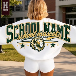 Może przedstawiać: Biała bluza z długim rękawem z napisem SCHOOL NAME dużymi ciemnozielonymi literami blokowymi oraz school mascot złotą kursywą. Grafika przedstawiająca głowę lwa znajduje się pod tekstem, otoczona dwiema ciemnozielonymi gwiazdami na białym tle.