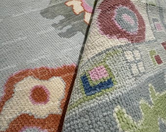 May include: A section of a light blue rug with a floral pattern in shades of pink, orange, green, and gray. The rug is partially rolled up, revealing the underside and texture. The rug has a soft, woven texture.