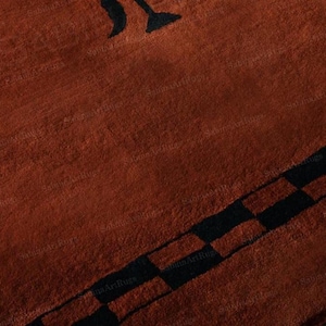 May include: A close-up of a rust-colored rug with a black geometric design. The rug has a textured surface and a black border with a checkered pattern. A black abstract shape is visible in the upper left corner.