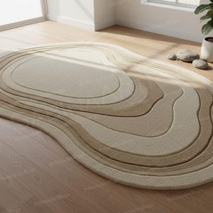 Könnte beinhalten: Ovaler Teppich mit einem geschichteten, topografischen Design. Der Teppich hat eine Palette aus Beige- und Brauntönen, die eine weiche, neutrale Ästhetik erzeugt. Das Design des Teppichs ähnelt einer Konturkarte und sorgt für visuelles Interesse.