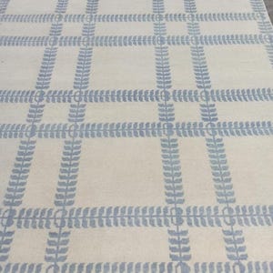 May include: A rectangular area rug with a cream-colored background and a repeating pattern of light blue leaf-like designs. The pattern forms a grid-like structure across the rug's surface. The rug has a soft, inviting appearance.
