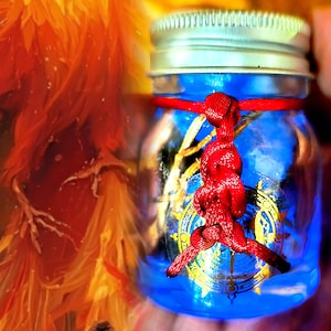 Puede incluir: Un pequeño tarro de cristal con tapa plateada, lleno de líquido azul y un diseño dorado y azul. Una cuerda roja está atada alrededor del tarro. El fondo tiene tonos naranja y amarillo.