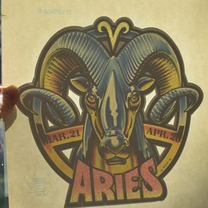 May include: Aries zodiac sign sticker featuring a ram with large curved horns. The sticker has a retro design with the dates MAR. 21 and APR. 20. The word ARIES is in a stylized font.