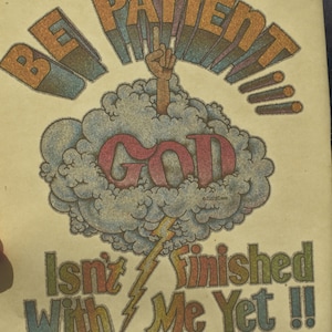 May include: Vintage poster with the words "BE PATIENT" in orange and blue, above a cloud with the word "GOD" in red. A hand reaches out from the cloud. The text "Isn't Finished With Me Yet !!" is below.
