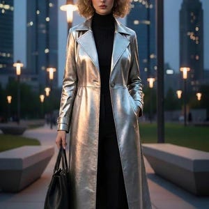 Könnte beinhalten: Ein silberner metallischer Trenchcoat mit schwarzem Rollkragenpullover und schwarzer Hose. Der Mantel hat ein klassisches Revers und einen Knopfverschluss. Eine schwarze Handtasche wird in der linken Hand gehalten. Der Hintergrund zeigt Stadtlichter und Gebäude.